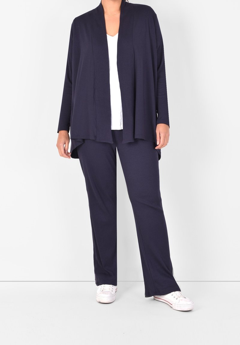 Marinblå stickad kofta med öppen framsida, långa ärmar, matchad med ribbade byxor. Vit V-ringad topp under och vita sneakers.