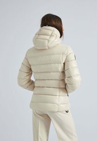 Beige dunjakke med hætte, der har et quiltet design, lynlåslommer og en let figursyet silhuet. Glat, skinnende tekstur.