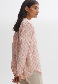Long-sleeve shirt made of lightweight fabric featuring a checkered pattern in red and beige, with a relaxed fit and rounded hem.