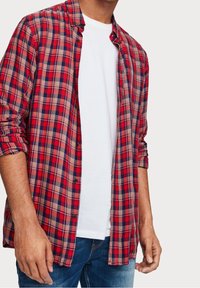 Rood en marineblauw geruit overhemd met lange mouwen, opgerolde mouwen, knoopsluiting aan de voorkant, gedragen over een wit T-shirt, gecombineerd met blauwe jeans.
