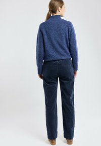 Pull en tricot bleu marine avec un col montant, associé à un pantalon en velours côtelé bleu marine foncé. La texture est douce et lisse, avec une coupe décontractée.