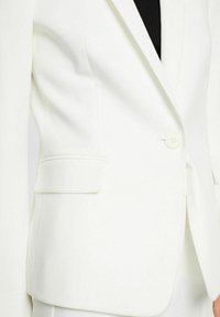 Biała dopasowana marynarka z jednym guzikiem do zapięcia, lewą kieszenią na piersi oraz gładką fakturą tkaniny. Klasyczny design z uporządkowaną sylwetką.
