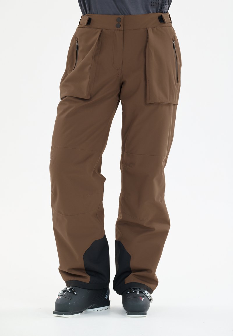 Bruine skibroek van duurzaam materiaal met een losse pasvorm, voorzien van twee zijzakken, een ritszak en zwarte accenten aan de onderkant van de benen.