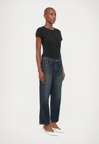 Top negro ajustado de manga corta combinado con jeans de pierna recta de cintura alta en azul oscuro. La modelo lleva zapatos blancos de punta. Diseño minimalista.