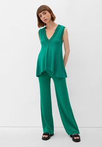 Groene mouwloze top met een diepe V-hals, gecombineerd met ruime broek in bijpassende kleur. Beide gemaakt van zachte, lichte stof. Zwarte platform sandalen.