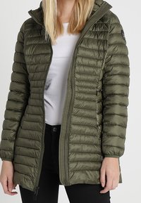 Grøn isoleret pufferjakke med horisontal quiltet design, front lynlås og hætte. Glat, skinnende tekstur med et logo-patch på ærmet.