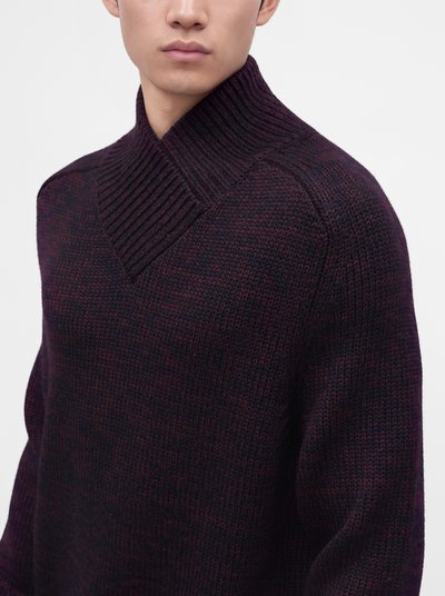 Homme portant un pull tricoté texturé foncé avec un large col châle côtelé sur un fond clair uni.