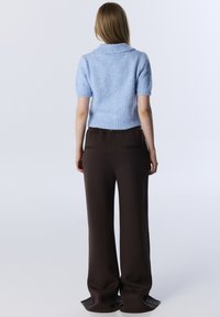 Kortarmige lichtblauwe trui met een brede kraag, gecombineerd met donkerbruine brede broek met zijzakken en een soepele structuur.