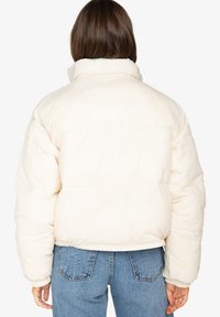 Crème-kleurige pufferjack met hoge kraag, boxy pasvorm en elastische manchetten. Heeft een gewatteerde textuur en een cropped lengte.