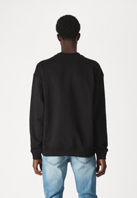 Črni pulover s krožnim izrezom, narejen iz mešanice bombaža, z rebrastimi manšeti in robom, sproščenega kroja ter brez vidnih detajlov na hrbtu.