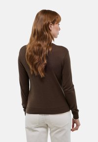 Pull à manches longues marron foncé avec un design ajusté et des poignets côtelés, porté avec un pantalon texturé de couleur claire. Vue de dos.