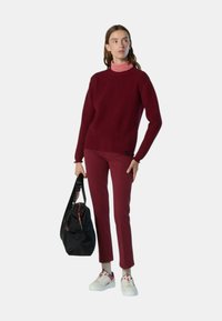 Maglione testurizzato borgogna, dolcevita rosa sotto, abbinato a pantaloni a sigaretta bordeaux, sneakers bianche e una borsa a tracolla nera.