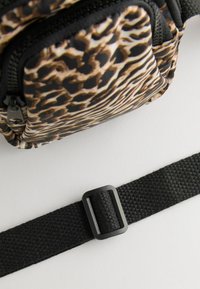 Taška s leopardím vzorom a lesklým povrchom, ktorá má dve vrecká na zips, čierne zipsy a čierny popruh s obdĺžnikovou plastovou prackou.