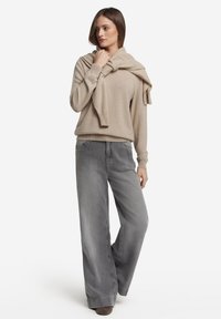 Beżowy sweter z okrągłym dekoltem zarzucony na ramiona, zestawiony z szarymi dżinsami o szerokich nogawkach. Oba elementy charakteryzują się miękkimi teksturami i luźnym krojem.