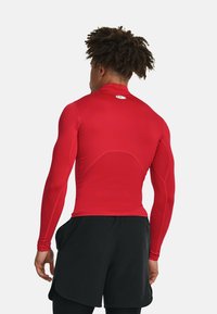 Rød, langærmet atletisk skjorte lavet af glat, strækbart stof. Har en høj krave og et lille logo på ryggen. Sæt den sammen med sorte shorts.