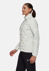 Ljust grått quiltat pufferjacka med hög krage, hel dragkedja fram, två sidofickor och logotypdetalj på ärmen. Slät textur.