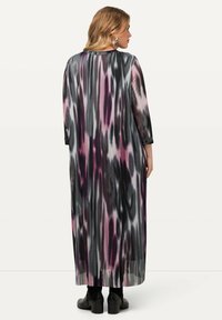 Maxi-jurk met lange mouwen, van lichtgewicht geplooid stof. Heeft een zwart, grijs en roze abstract patroon. Draagt met zwarte sleehaklaarzen.