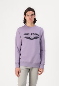 Sudadera lavanda con cuello redondo, con un estampado de logo negro y un diseño de alas en la parte frontal. Mezcla de algodón, puños y dobladillo acanalados.