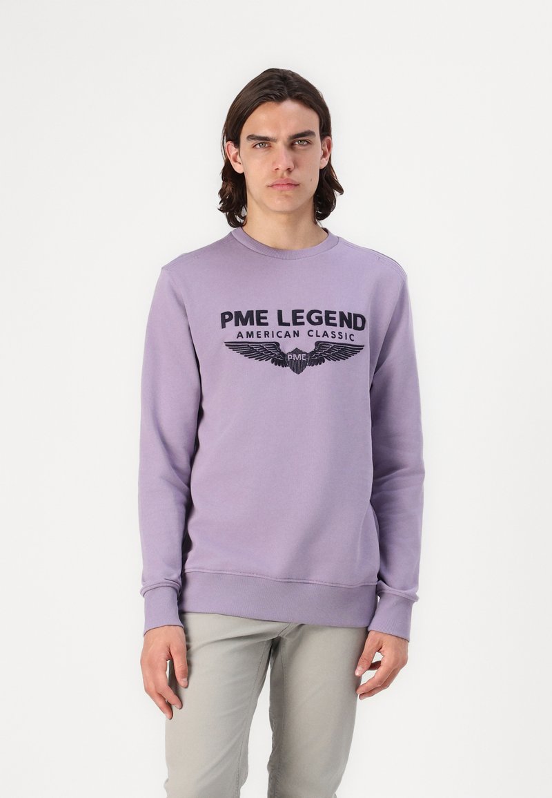 Sudadera lavanda con cuello redondo, con un estampado de logo negro y un diseño de alas en la parte frontal. Mezcla de algodón, puños y dobladillo acanalados.