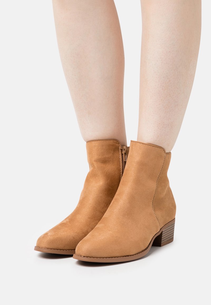 Beżowe botki zamszowe z gładkim wykończeniem, zaokrąglonym noskiem i niskim, piętrowym obcasem. Zamek błyskawiczny z boku, brak widocznych wzorów.