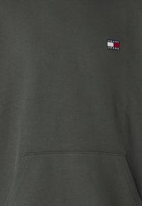 Felpa in cotone verde scuro con tasca frontale, caratterizzata da un piccolo logo ricamato "Tommy Jeans" in rosso, bianco e blu navy.