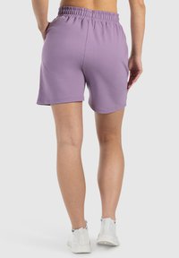 Shorts in cotone viola con vita elastica, taglio dritto e texture liscia, abbinati a scarpe da ginnastica bianche.