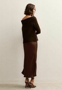 Brown off-the-shoulder sweater with a textured knit, paired with a brown satin slip skirt featuring a side slit, and strappy high-heeled sandals.