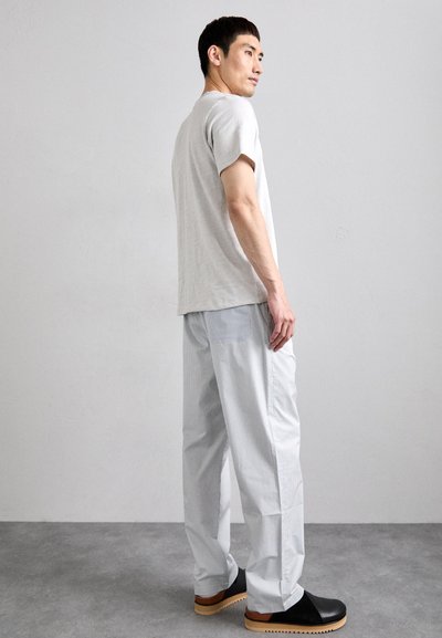 T-shirt gris clair à manches courtes associé à un pantalon bleu à rayures, ample, et des chaussures noires à enfiler avec une semelle en bois.