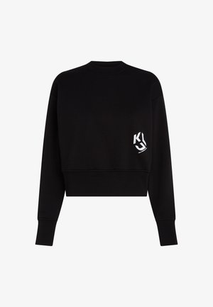 Must mustkas pikkusega musta värvi pehme kangast sviiter, millel on ümmargune kaelus ja pikad varrukad. Vasakul rinnal on valge logo.