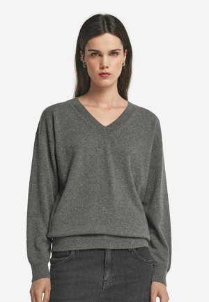 Pull gris à col en V en tissu doux, doté d'une coupe décontractée et d'un ourlet côtelé. Les manches longues créent une silhouette confortable et décontractée.