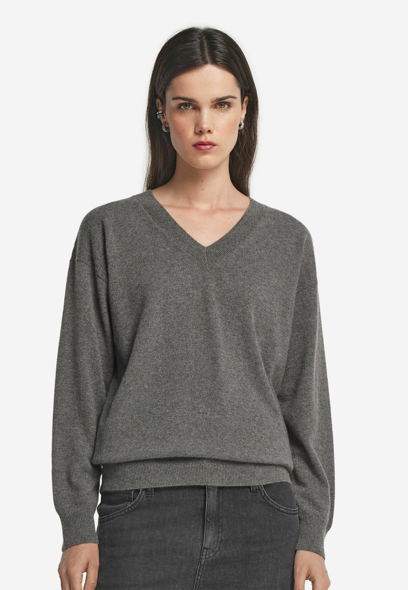 Grauer V-Ausschnitt-Pullover aus weichem Stoff, mit lockerem Schnitt und geripptem Saum. Lange Ärmel schaffen eine bequeme, lässige Silhouette.
