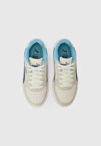 Sneaker beige e navy con materiale testurizzato. Presentano dettagli in azzurro chiaro, punta perforata e suola in gomma bianca. I lacci sono infilati in modo uniforme.