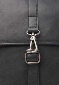 Bolso de hombro de cuero negro con un cierre de metal plateado, superficie texturizada y costura resistente a lo largo de la correa y el cuerpo.