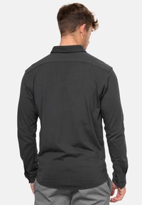 Camisa de manga larga gris oscuro con cuello abotonado, que presenta una textura suave, un corte ajustado y detalles de botones en los puños.