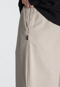 Pantalons en coton beige avec une coupe décontractée, dotés de poches latérales et d'une petite étiquette noire sur la taille. Tissu texturé.