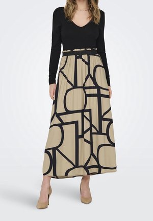 Femme portant un haut noir à manches longues et une jupe maxi beige avec des motifs géométriques noirs audacieux et des chaussures à talons beiges.