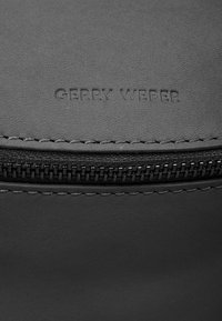 Borsa a mano in pelle grigia con logo "GERRY WEBER" in rilievo. Presenta una superficie texturizzata, cuciture visibili e una chiusura con zip con accenti scuri.