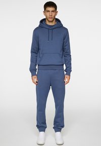Blå träningsoutfit som består av en huoodad sweatshirt med framficka och matchande joggers. Tillverkad av mjukt material med ribbade ärmar.
