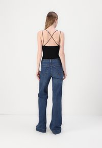 Svart bodysuit med kryssende stropper, kombinert med blå vide jeans med fem-lommers design og synlige sømdetaljer.