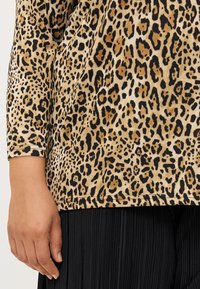 A close-up of a hand resting on a leopard-print fabric, featuring black and tan spots, alongside a black pleated garment.