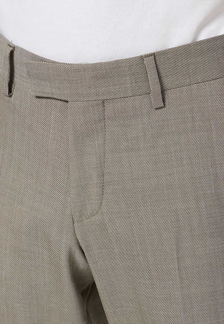 Pantalons tissés beiges avec une taille plate, des poches latérales et un tissu texturé. La ceinture comporte des passants pour une ceinture.