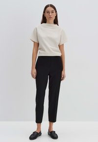 Pantaloni neri su misura con una vestibilità slim, abbinati a un top testurizzato bianco sporco con collo alto e maniche corte. Scarpe slip-on nere.