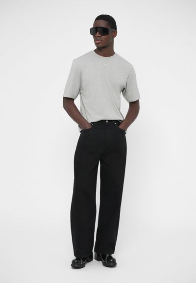 Sivá tričko s krátkym rukávom, čierne nohavice s rovnými nohavicami, čierne veľké slnečné okuliare a čierne topánky, minimalistický dizajn s ležérnym strihom.