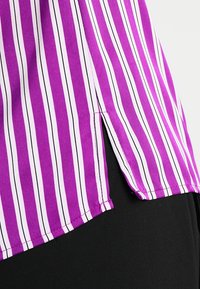 Purple and white striped shirt featuring a side slit and a smooth fabric texture. The garment has a straight hem and well-finished seams.