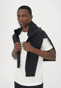 Navy sweatshirt draped over a white short-sleeve shirt. The sweatshirt has ribbed cuffs and a relaxed fit, with a soft texture.