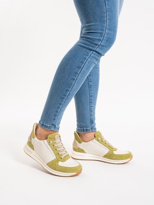 Legs wearing blue skinny jeans and white sneakers with light green suede accents, standing on a white background.