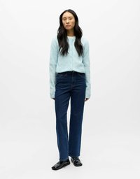 Svijetloplavi kardigan s gumbima upareni s tamnoplavim trapericama. Model nosi crne mokasine. Jednostavan dizajn, glatka tekstura.