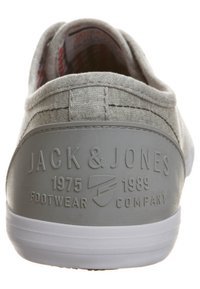 Šedá plátěná nazouvací bota s bílou gumovou podrážkou. Na zadní straně je vyražený text: "JACK & JONES 1975 FOOTWEAR 1989 COMPANY."