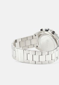 Reloj de acero inoxidable con un diseño de pulsera de eslabones en plata. Presenta una caja redonda, botones negros y un logo grabado en la pulsera.