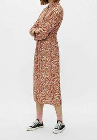 Abito midi floreale in tonalità arancioni, rosa e verdi; design con bottoni e maniche lunghe; abbinato a sneakers nere e calzini a pois rosa.